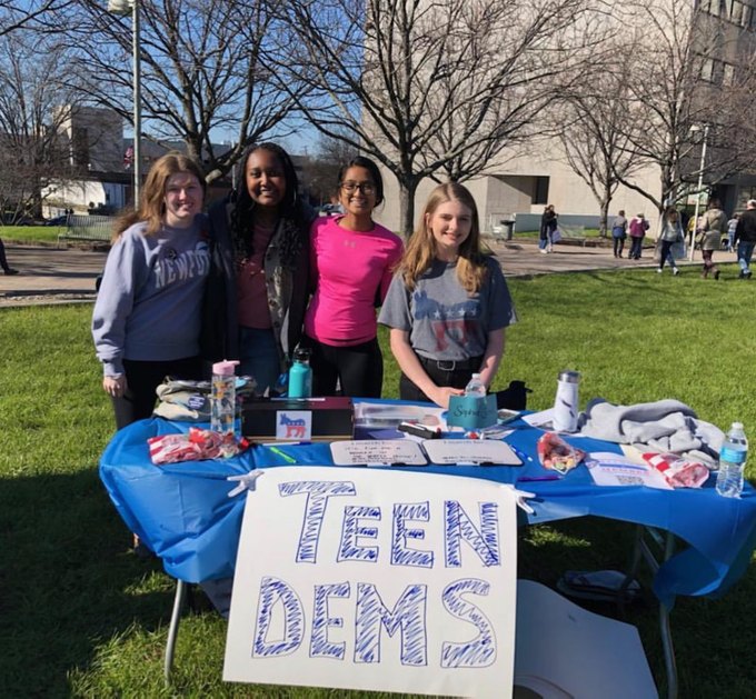 Four Teen Dems members behind a blue outreach table at the Women’s March